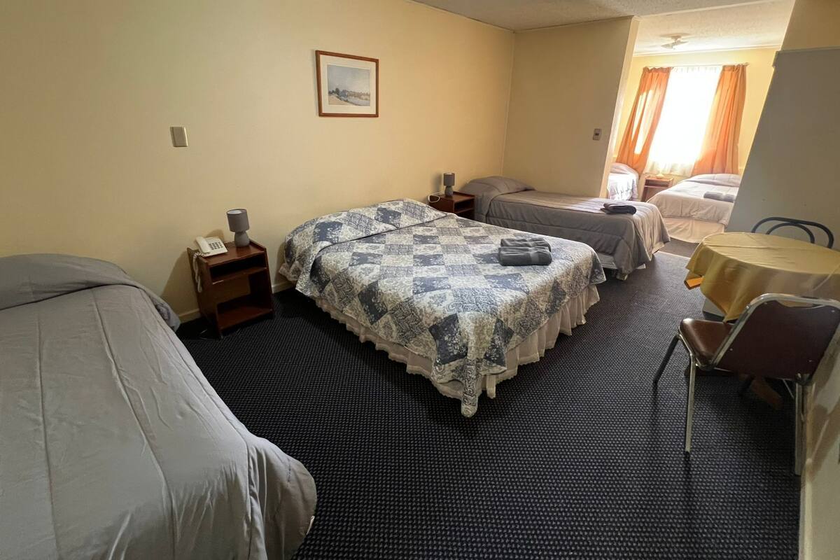 Habitación de hotel con dos camas, una mesita, una silla, un escritorio y un cuadro en la pared.
