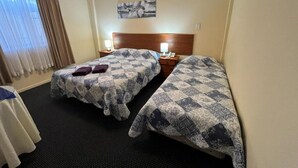 Habitación de hotel con dos camas, cabecero, mesita de noche, lámpara y ventana con cortinas.
