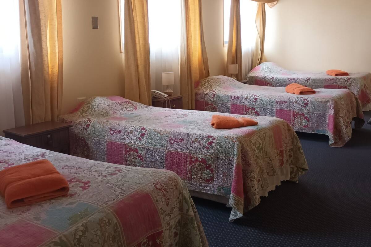 Habitación de hotel con tres camas, cada una con una colcha estampada y una toalla naranja.