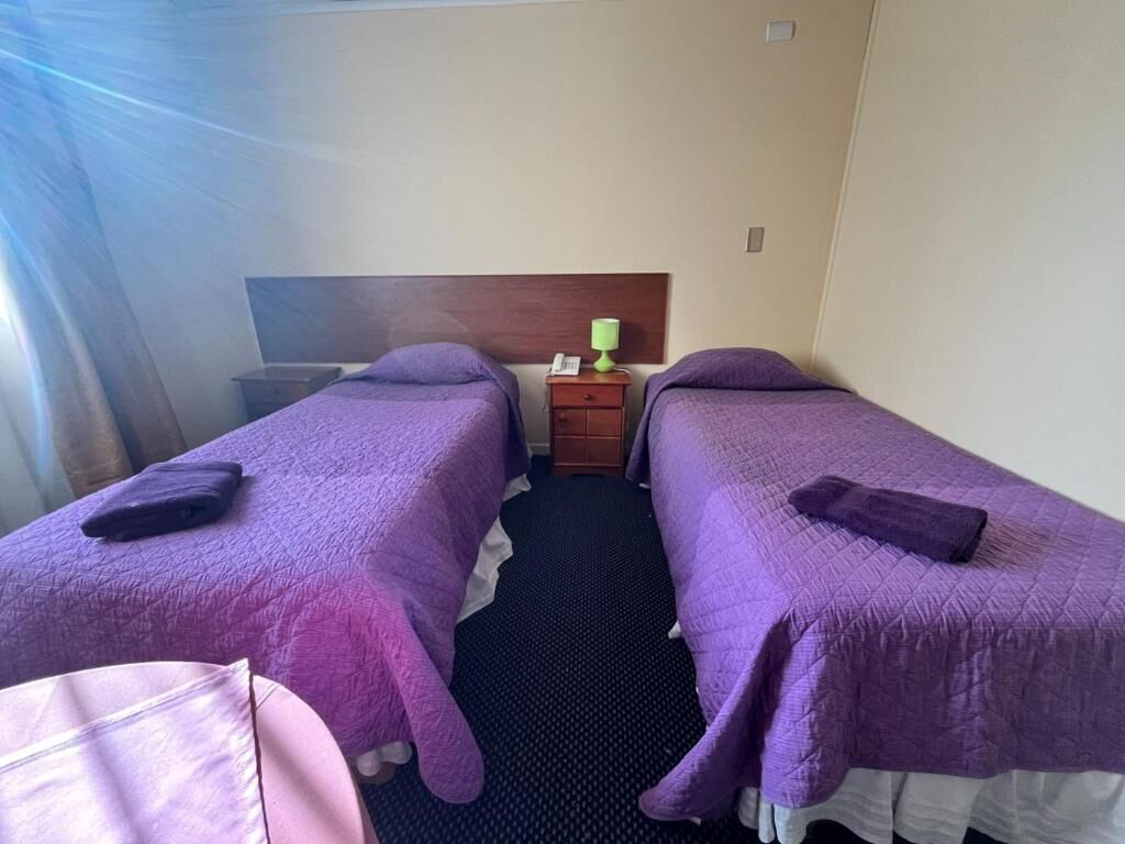 Ein Hotelzimmer mit zwei Betten, einem Nachttisch, einer Lampe und einem Fenster mit Vorhängen.