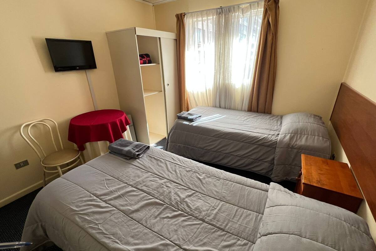 Habitación de hotel con dos camas, televisión, armario, silla y una pequeña mesa.