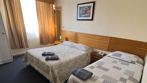 Habitación de hotel con dos camas, una mesita de noche con lámpara, un cuadro enmarcado en la pared y una ventana con cortinas.