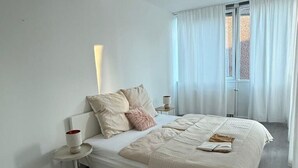 A modern bedroom with a bed, bedside tables, and a view through a window.