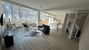 A spacious living room with a large window, a black sofa, a white chair, and a staircase.