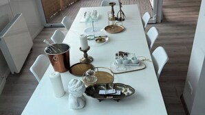 A dining table set with white chairs, a copper pot, a candle, and various glassware.