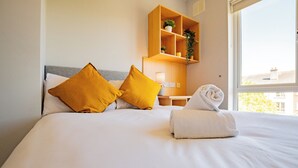 A hotel room with a bed, two pillows, a bedside table with a lamp, a shelf with plants, and a window. - Spacious Townhouse by Shortstays (Gaillimh)