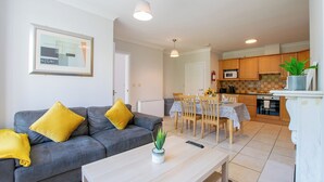 A modern living room with a grey sofa, yellow cushions, a white coffee table with a plant, and a dining area with a wooden table and chairs. - Spacious Townhouse by Shortstays (Gaillimh)