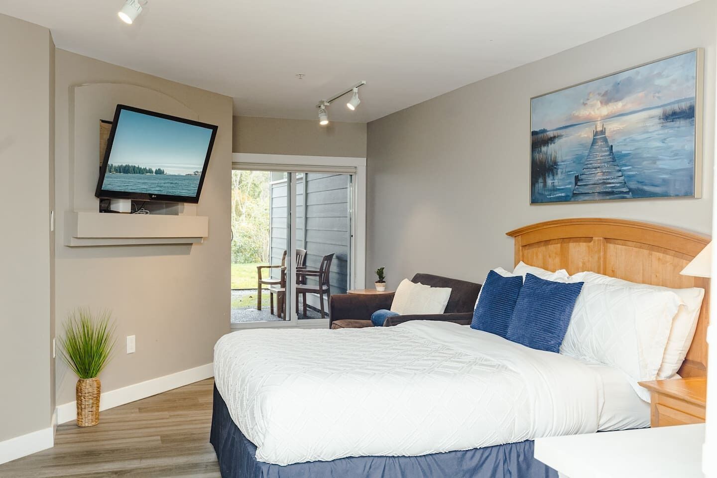Une chambre à coucher avec un lit, un téléviseur fixé au mur, un tableau au-dessus du lit et une vue sur l’extérieur grâce à une porte coulissante.