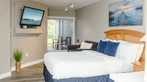 Een slaapkamer met een bed, een aan de muur bevestigde televisie, een schilderij boven het bed, en uitzicht op de omgeving door een schuifdeur.
