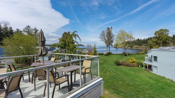 Um terraço com mobiliário de exterior, vista para um lago e uma casa ao fundo.