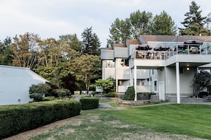 Un bâtiment à deux étages doté d’un balcon et d’un espace extérieur aménagé pour s’asseoir, le tout entouré d’un jardin bien entretenu.