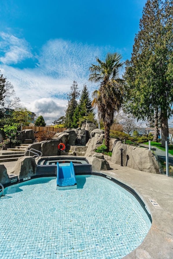 Une piscine avec un toboggan, entourée de rochers et de palmiers.