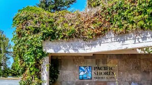 A entrada do Pacific Shores Resort & Spa, com uma placa, um caminho pavimentado e vegetação.