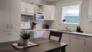 Una cocina moderna con armarios blancos, un microondas, una estufa, un fregadero y una ventana.