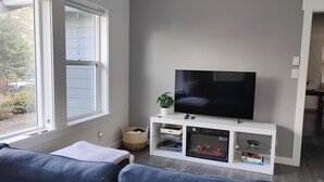 Una sala de estar con televisor, mueble blanco de entretenimiento y un sofá.