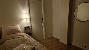 Une chambre à coucher avec un lit, une lampe de chevet, une porte et un miroir fixé au mur.
