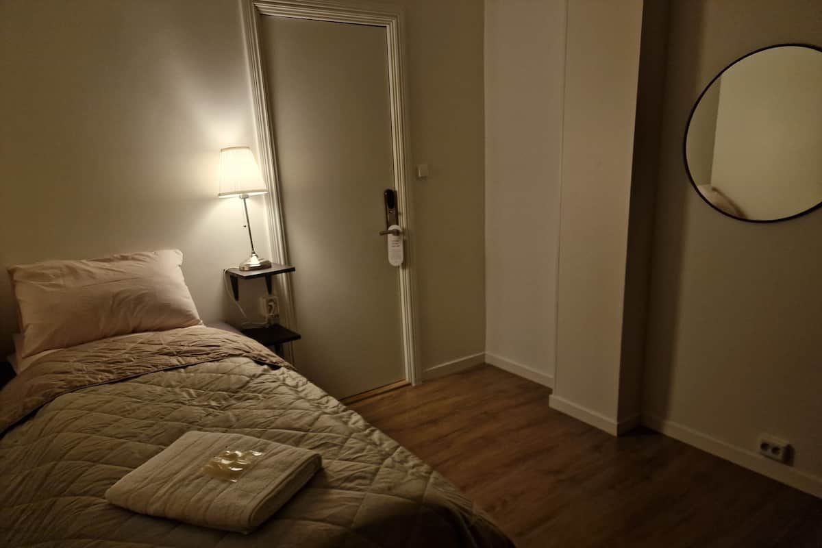 A bedroom with a bed, a bedside lamp, a door, and a wall-mounted mirror.