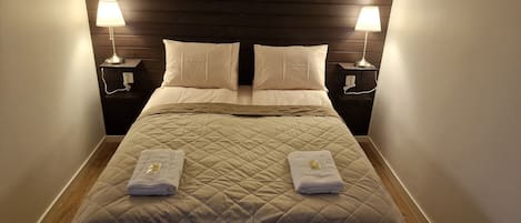A neatly made bed with a quilted headboard, two bedside lamps, and two folded towels on the footboard.