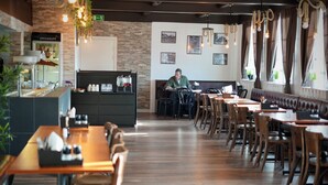 Un restaurant avec des tables et des chaises en bois, un comptoir où sont servis les boissons, et des tableaux encadrés accrochés au mur.