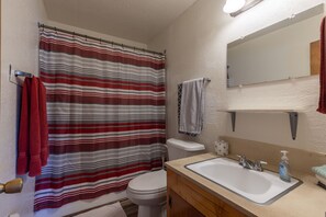 Ein Badezimmer mit gestreiftem Duschvorhang, Toilette, Waschbecken mit Spiegel und zwei Handtüchern, die an der Wand hängen.