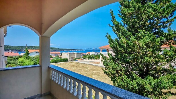 Een balkon met uitzicht op een kustgebied, inclusief huizen en een helderblauwe lucht.