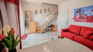 Ein Wohnzimmer mit einem roten Sofa, einem Marmortisch, einer Treppe und einem Gemälde an der Wand.