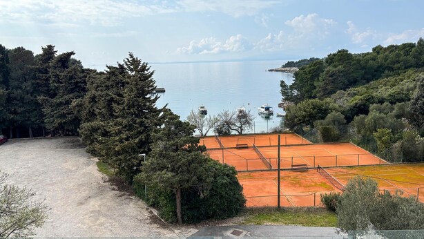 A tennis court with a view of a lake and surrounding trees. - Gorgeous apartment in Rab with house sea view (Rab)
