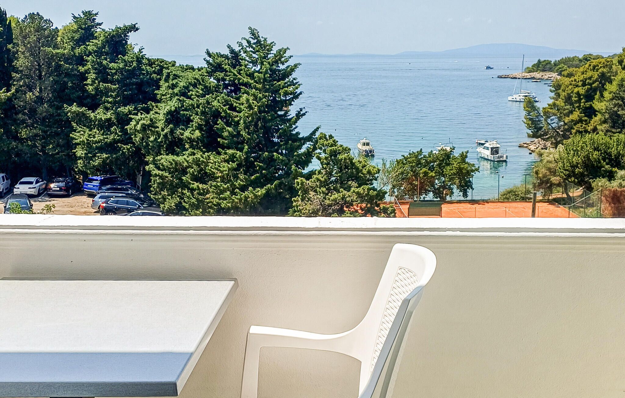 A balcony with a view of a body of water, boats, and parked cars.