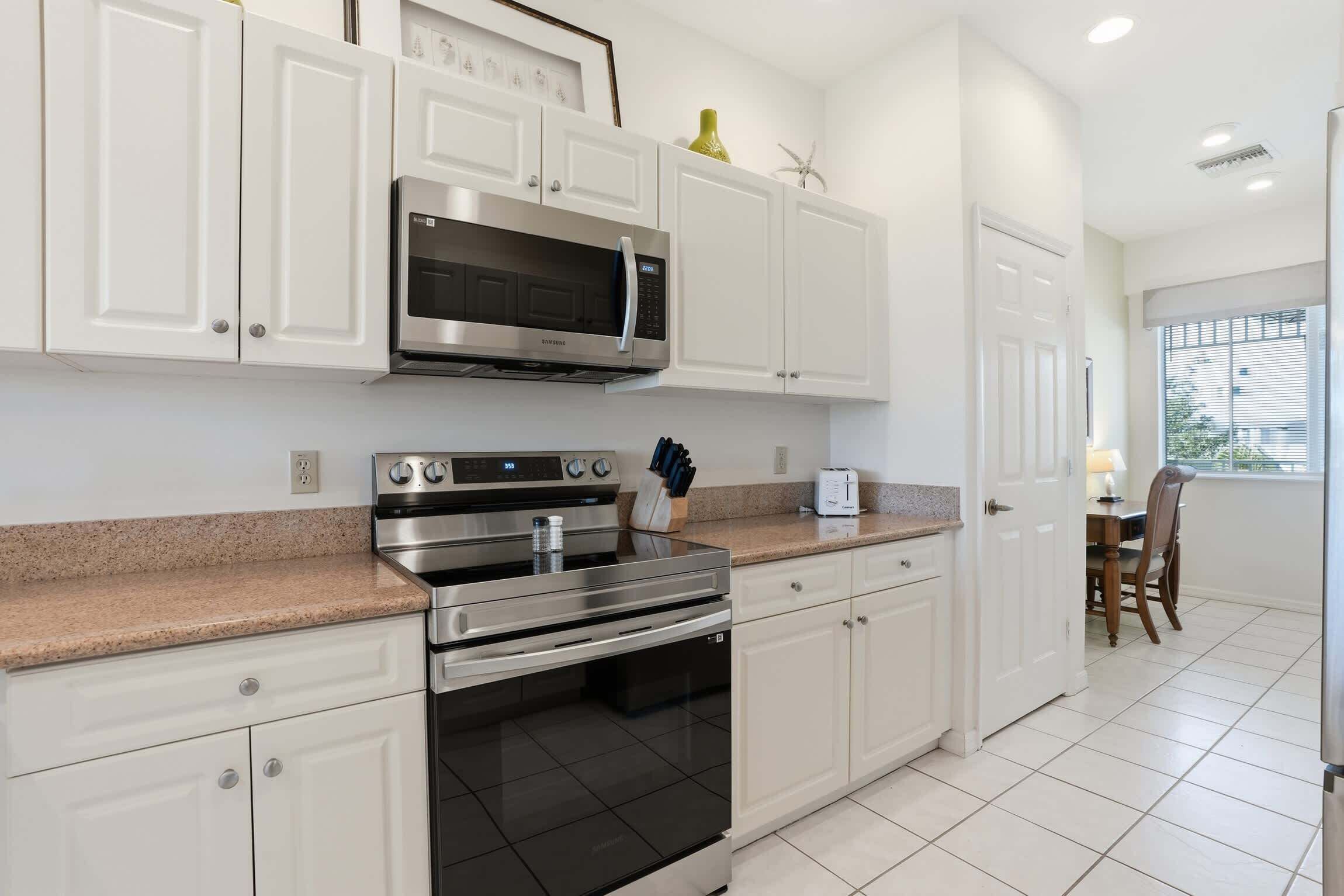 A kitchen with white cabinets, a microwave, an oven, and a dining area with a table and chairs.