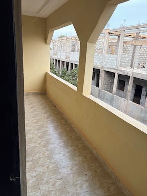 Un balcón con suelo de baldosas, vista a una obra en construcción y una pared lisa.