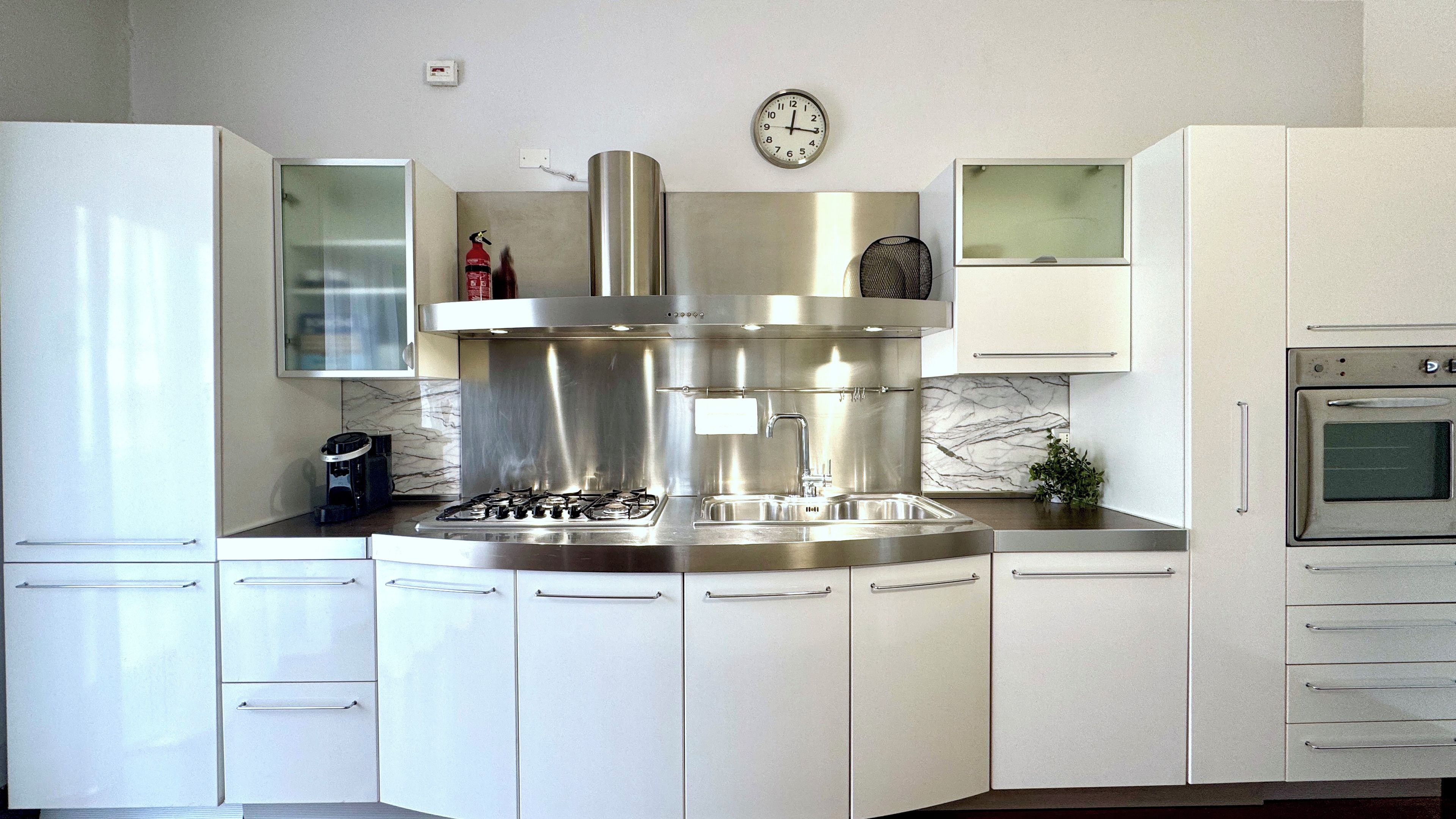 Una cucina moderna con cappa in acciaio inossidabile, forno integrato e un orologio a parete.