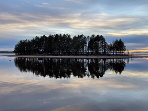 A calm lake with a reflection of trees and a clear sky.