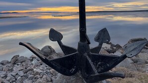 An anchor on a rocky shore with a calm body of water and a cloudy sky in the background. - Villa Heed (Tallberg)