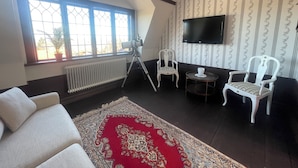 A room with a large window, a telescope, two white chairs, a small round table, and a mounted TV. - Villa Heed (Tallberg)