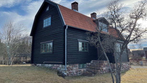 A black wooden house with a red roof, stone foundation, and a small porch. - Villa Heed (Tallberg)