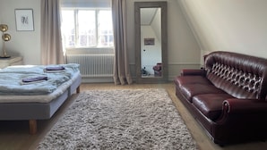A bedroom with a bed, a large mirror, a brown leather sofa, a fluffy rug, and a radiator. - Villa Heed (Tallberg)
