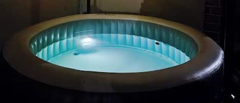 A hot tub with a light blue interior, surrounded by walls with a textured pattern and a ceiling with string lights.