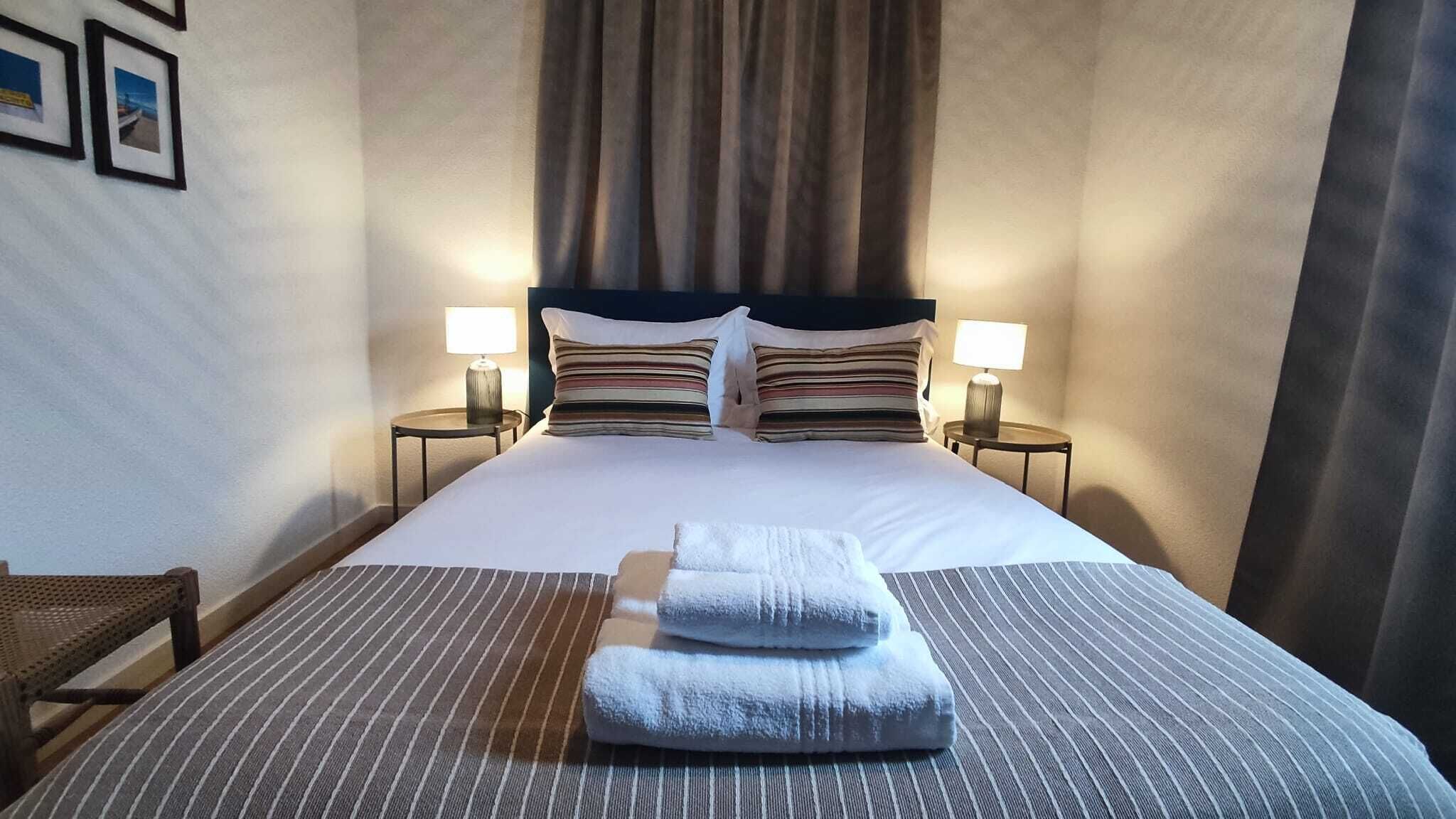 Et hotelværelse med en stor seng, to sengeborde med lamper, en stol og havudsigt gennem vinduet.