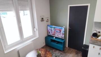 A living room with a TV, a coffee machine, a small table with a plant, and a door.