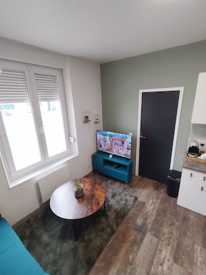A living room with a TV, a coffee machine, a small table with a plant, and a door. - Petit Cocon Near NEOMA / Stade Auguste Delaune (Reims)