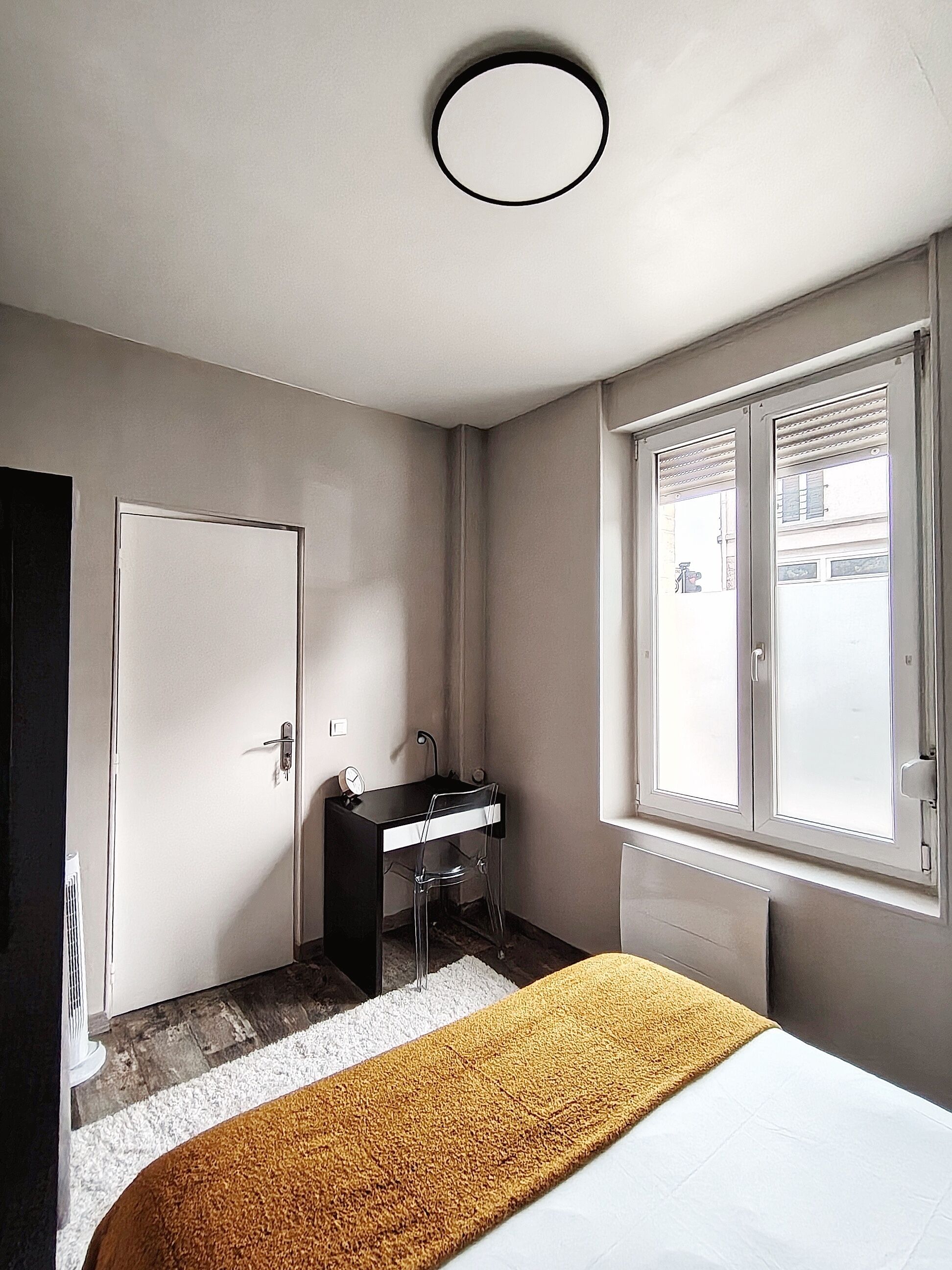 A bedroom with a bed, a desk with a chair, a window, and a door.