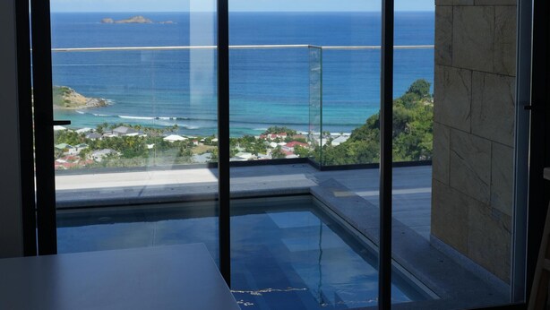 A room with a large sliding glass door leading to a balcony with a view of the ocean and a distant island.