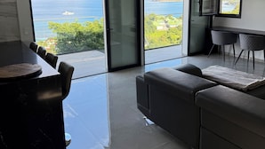 A modern living room with a large sliding glass door leading to a balcony with a view of the sea.
