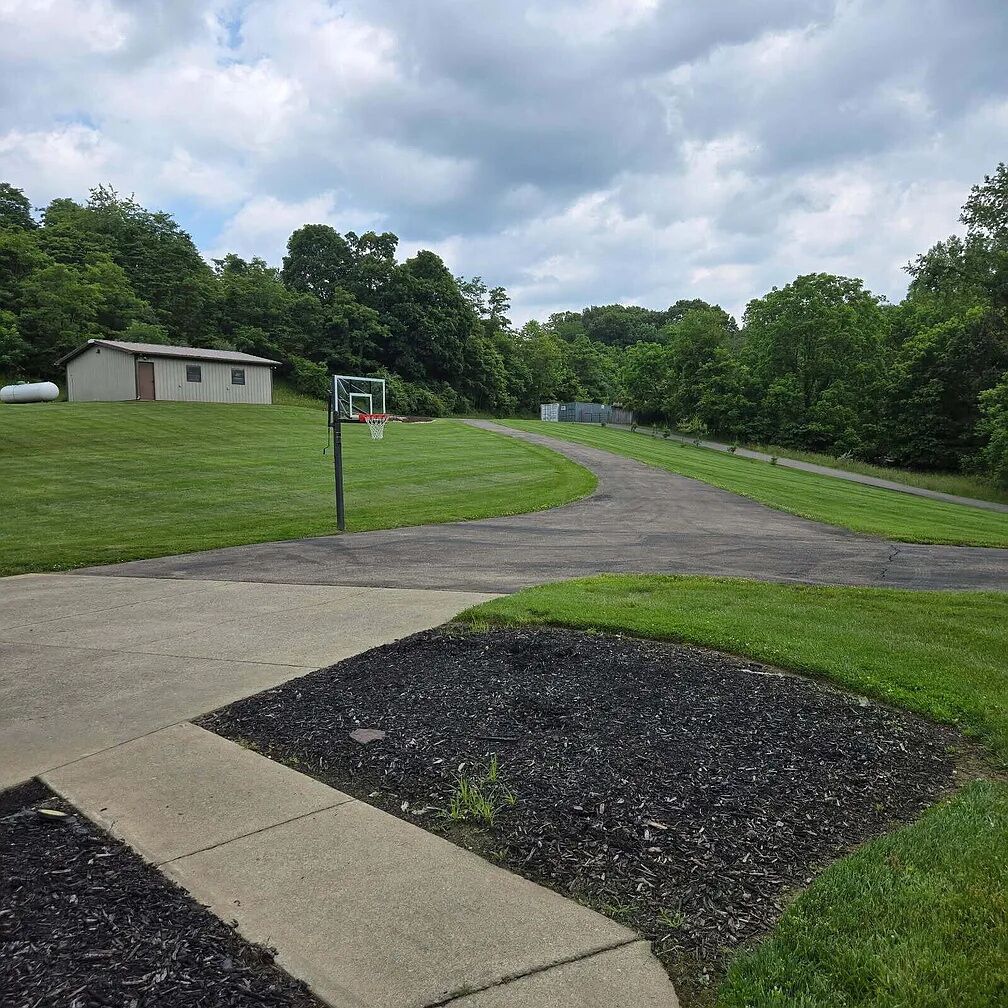 A basketball court with a hoop, a building, and a grassy area.