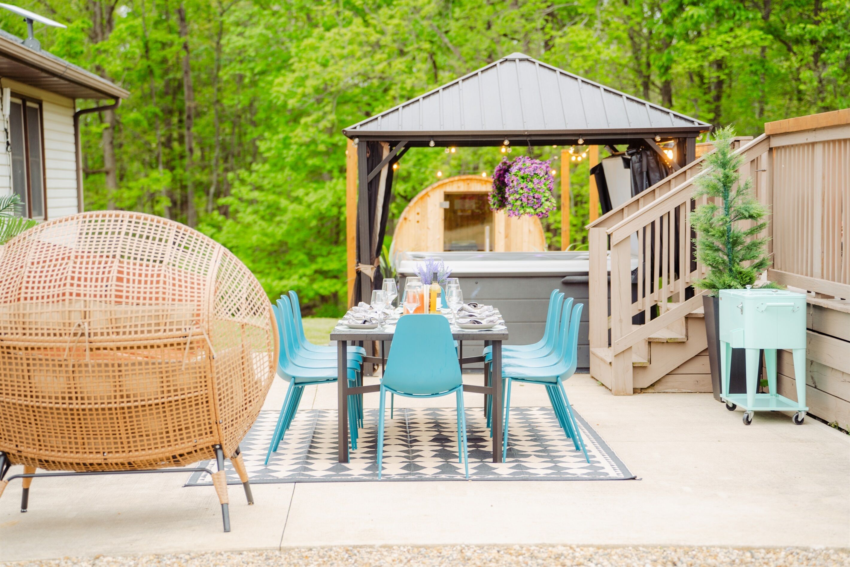 Een terras buiten met een tafel gedekt voor vier personen, omringd door rieten stoelen, een pergola en een houten terras.