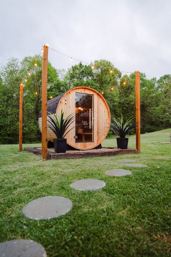 A wooden cylindrical structure with a door, surrounded by potted plants, and a string of lights.