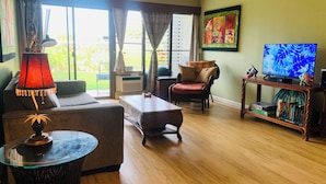 Ein Wohnzimmer mit Sofa, Sessel, Couchtisch, Fernseher und Bücherregal.
