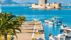 A coastal marina with boats docked, a fortified building, and palm trees along the waterfront. - AK Village Rooms - Peloponnese Comfy Gem (Nafplio)