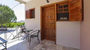 A balcony with a table and chairs, a wooden door with a window, and a wall-mounted light fixture. - AK Village Rooms - Peloponnese Comfy Gem (Nafplio)