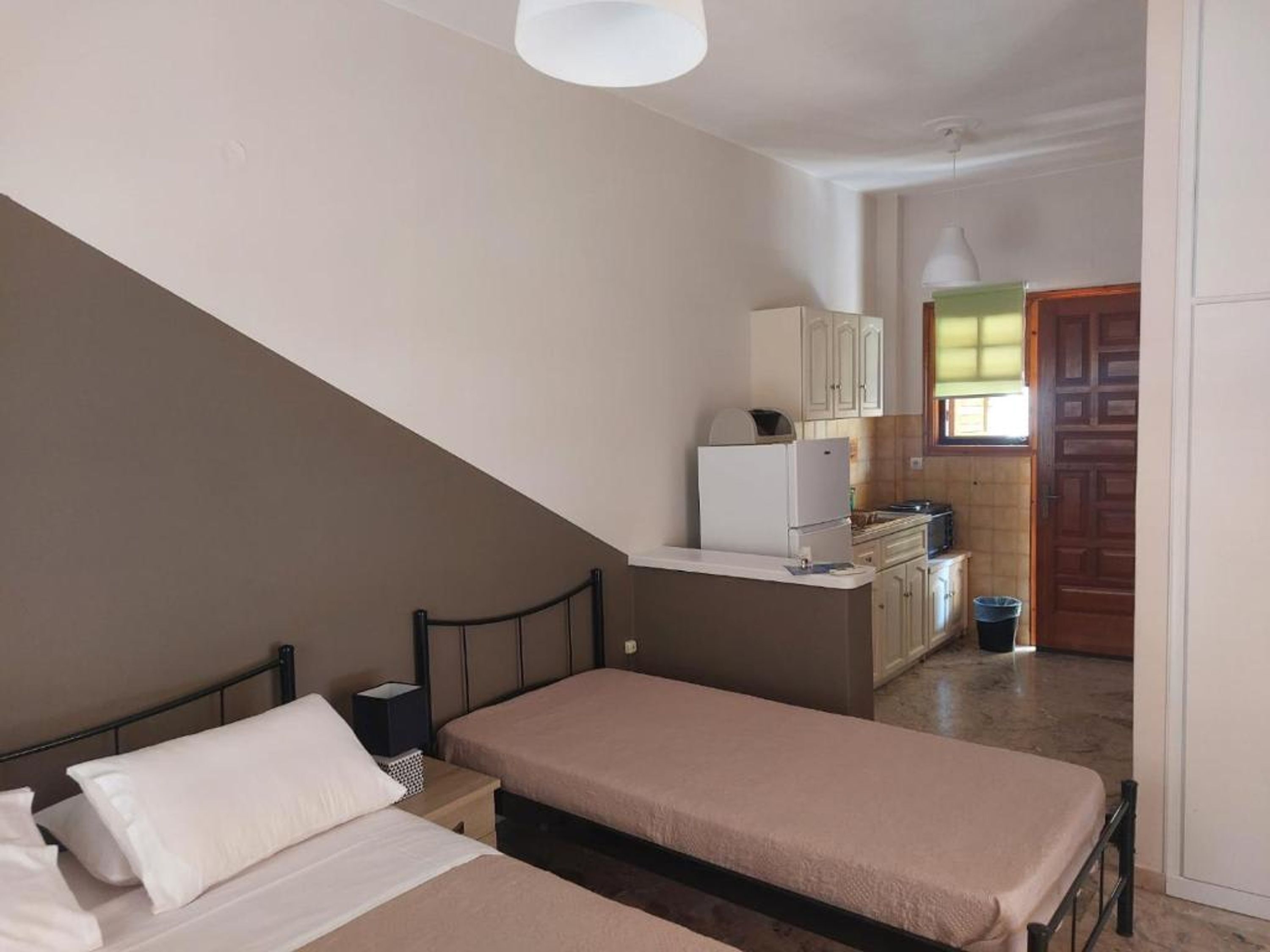 A bedroom with two beds, a kitchenette, and a bathroom.